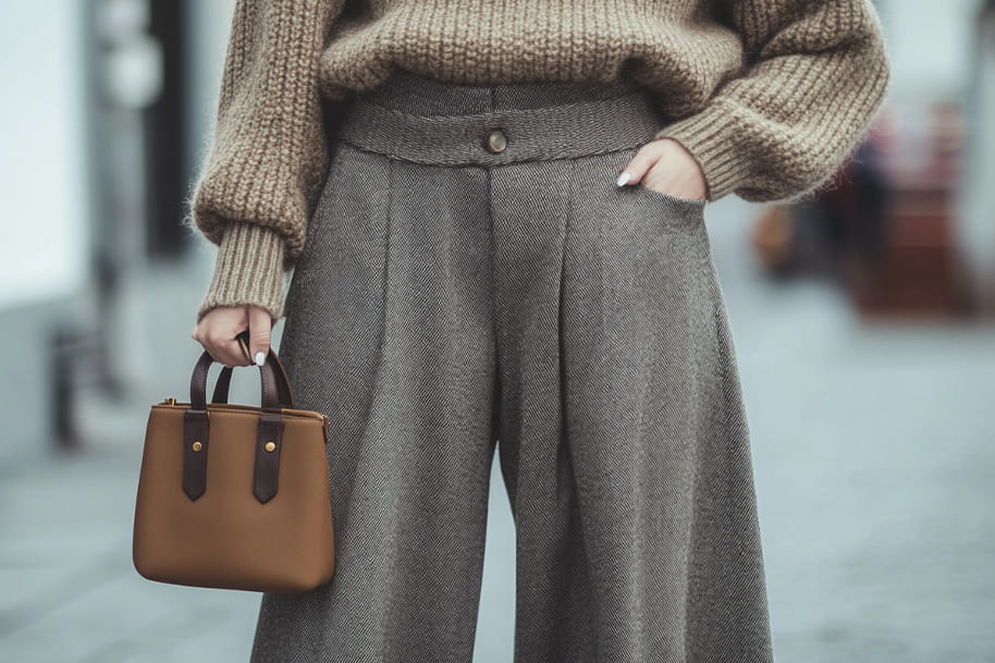 Elegant street-style fashion showcasing wide-leg tweed trousers paired with a cozy oversized knit sweater, complemented by a chic brown leather handbag, epitomizing timeless autumn and winter attire.