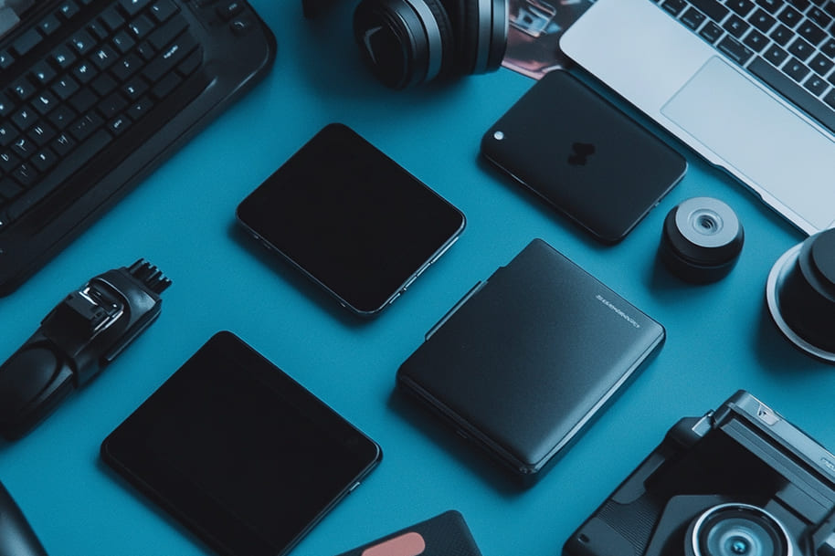 Flat lay of essential tech gadgets including smartphones, camera, keyboard, and accessories on a blue background – showcasing budget-friendly digital tools.