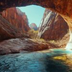 Stunning view from inside a red canyon cave opening toward turquoise river and dramatic rock formations in Zion National Park.