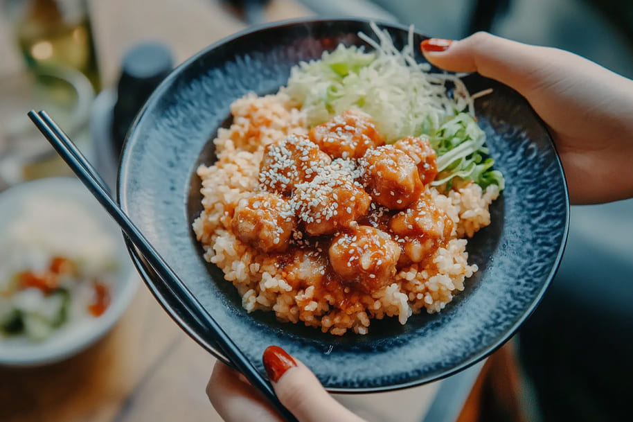 Close-up of Asian-style rice bowl with sesame chicken and fresh vegetables—highlighting trending TikTok food ideas for 2025 on EternalSlots.com blog
