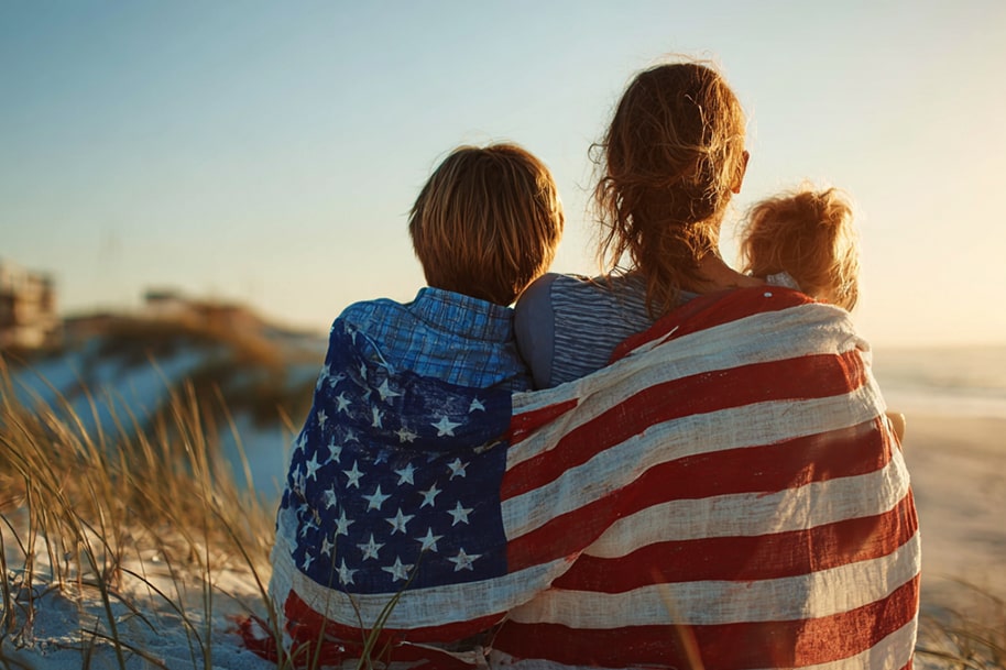 Family wrapped in American flag watching sunset on the beach during Independence Day vacation – featured in Eternal Slots Casino holiday blog post