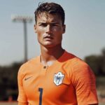 Confident male soccer player in orange jersey standing on a field – representing strength, focus, and the competitive edge in both sports and casino gaming