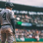 Baseball player wearing number 4 uniform, holding a bat and preparing to enter the game in a packed stadium.