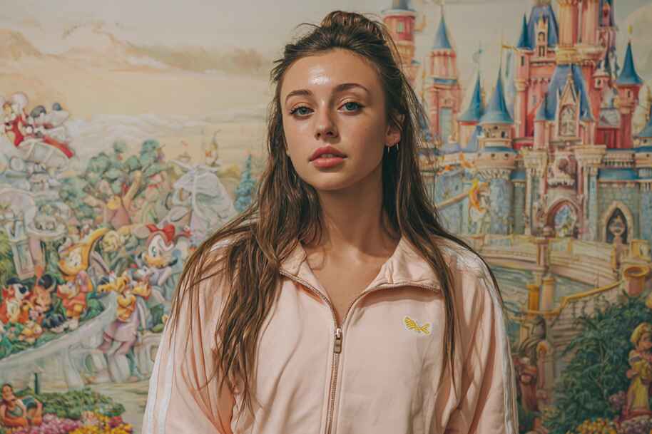 Popular American influencer in a light pink tracksuit posing in front of a colorful fairytale mural — featured on EternalSlots.com blog about influencer lifestyles, brand partnerships, and digital millionaire success stories.
