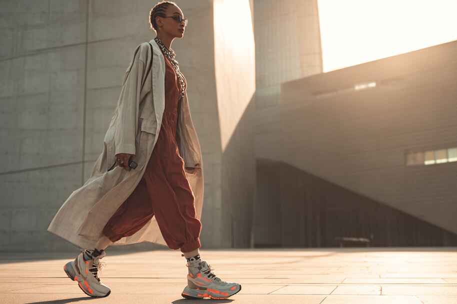 Stylish woman walking across a modern plaza in a flowy trench coat and tech-inspired jumpsuit.
