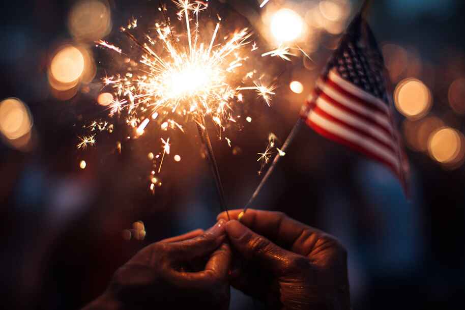 Close-up of hands holding a sparkler and American flag during Independence Day 2025 celebration – patriotic 4th of July moment featured on EternalSlots.com blog