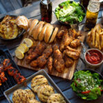 Best Labor Day cookout recipes with grilled chicken wings, BBQ skewers, burgers, fries, salads, and refreshing drinks on an outdoor table – perfect holiday food ideas for family and friends.