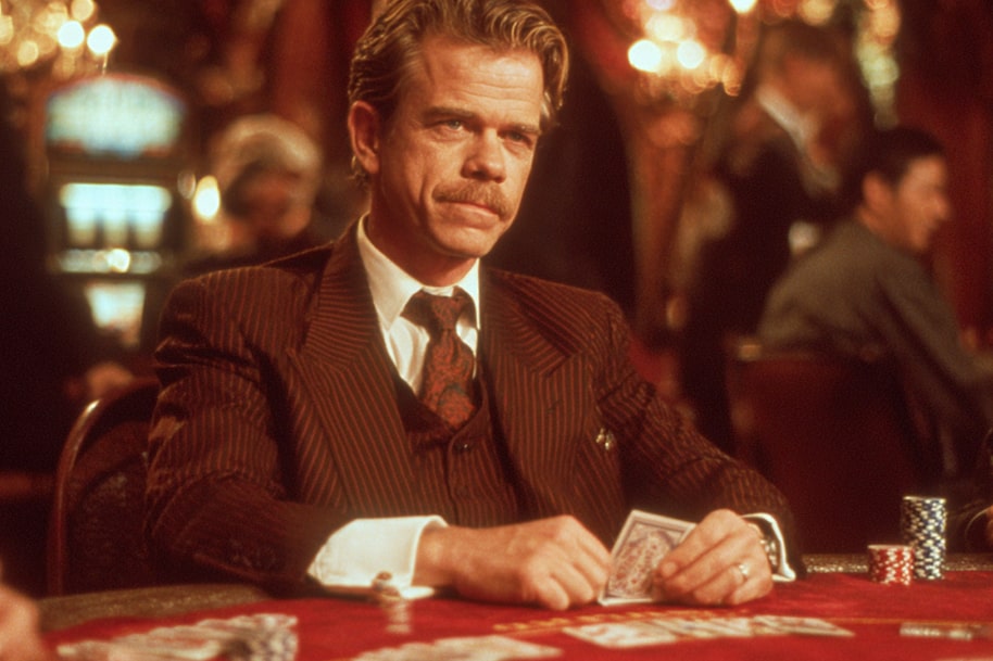 An intimate poker scene with the main character in a retro suit and a serious look, set in a warm, red-toned ambiance.