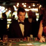 An elegant scene from the movie “21” with three players at a blackjack table. The focus is on the casino glamour and serious facial expressions, with the sparkling slot machines in the background.
