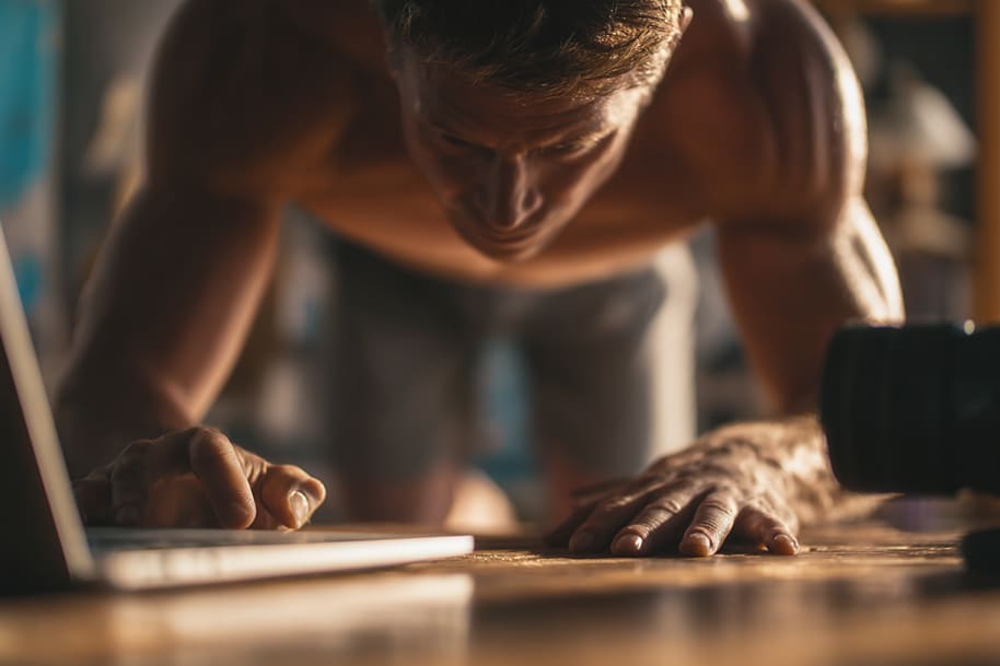 Remote worker doing push-ups at home while using laptop – combining fitness and productivity in a healthy remote work environment