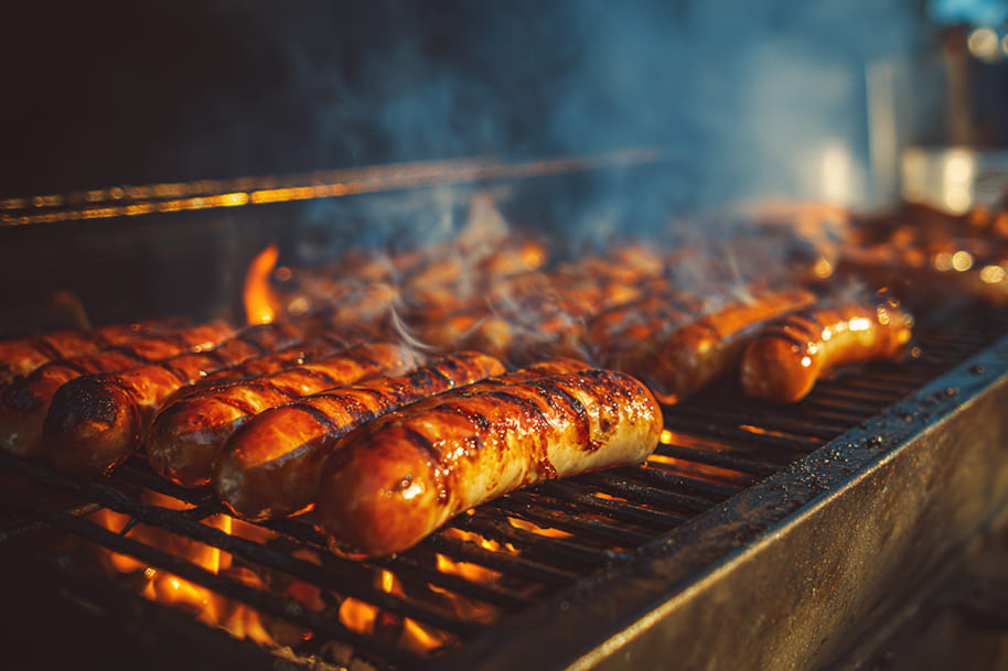 Grilled sausages cooking on a barbecue with flames and smoke, a popular Labor Day tradition in the US symbolizing family cookouts and holiday celebrations.