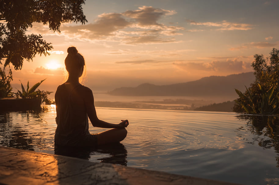Silhouette of woman meditating by infinity pool at sunset in Bali – yoga and meditation retreat for ultimate wellness travel escape.
