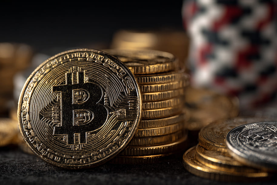 A close-up of a shiny gold Bitcoin standing upright against a stack of similar coins, symbolizing the rise of cryptocurrency in digital gambling.