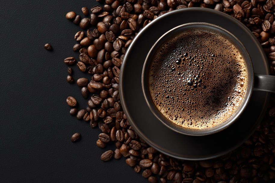 Top view of a dark coffee cup with frothy crema surrounded by roasted coffee beans – perfect visual for a blog on the best coffee alternatives for energy and focus at Eternal Slots Casino.