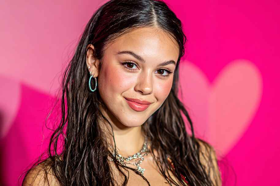 Olivia Rodrigo smiling at event with heart-shaped backdrop, reflecting her journey from Disney career to global fame, Eternal Slots casino blog article.