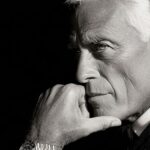 Black and white portrait of Giorgio Armani in a suit with a watch, thoughtful expression representing elegance, luxury, and timeless fashion.