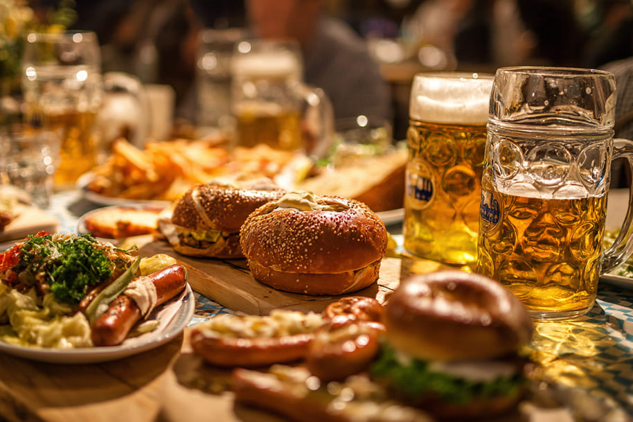 Oktoberfest celebration spread featuring sausages, pretzels, burgers, and frothy beer steins in a lively Bavarian atmosphere.