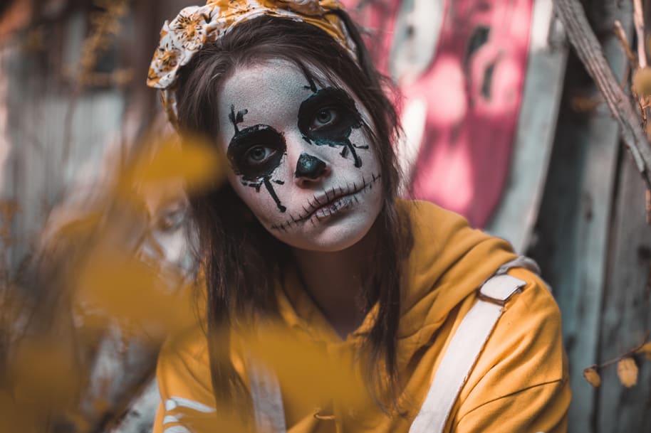 A woman wearing skeleton-style Halloween face paint and a yellow hoodie, symbolizing creative and easy Halloween costume ideas for 2025 featured on Eternal Slots Casino’s spooky season blog.
