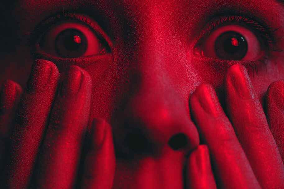 Close-up of shocked face lit in red light, symbolizing intense fear and emotional reaction explored in the psychology of fear.