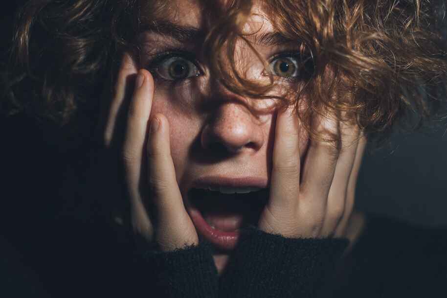 Frightened person holding face in panic, representing thrill-seeking behavior and how the brain processes fear in horror situations.