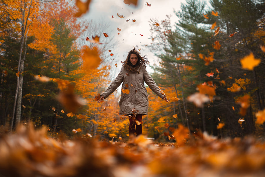 Woman walking through a forest surrounded by falling autumn leaves, capturing the beauty of October and the seasonal charm highlighted in the Eternal Slots Casino blog “Top Fall Activities to Try This October.”