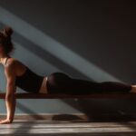 Young woman performing wall Pilates stretch on a wooden bench, focusing on core strength, flexibility, and mindful movement at home.